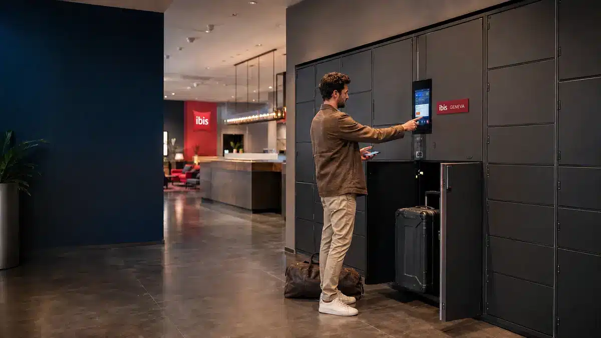 Hotel guest using the touchscreen on an Ibis Geneva smart luggage locker while storing a suitcase independently